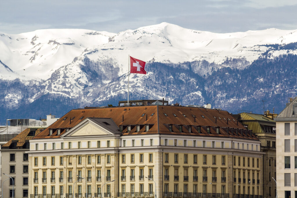 Facades of historic buildings in the city center of Geneva, Switzerland on the Leman lake with snow covered Alps mountains peaks in sunny clear day.